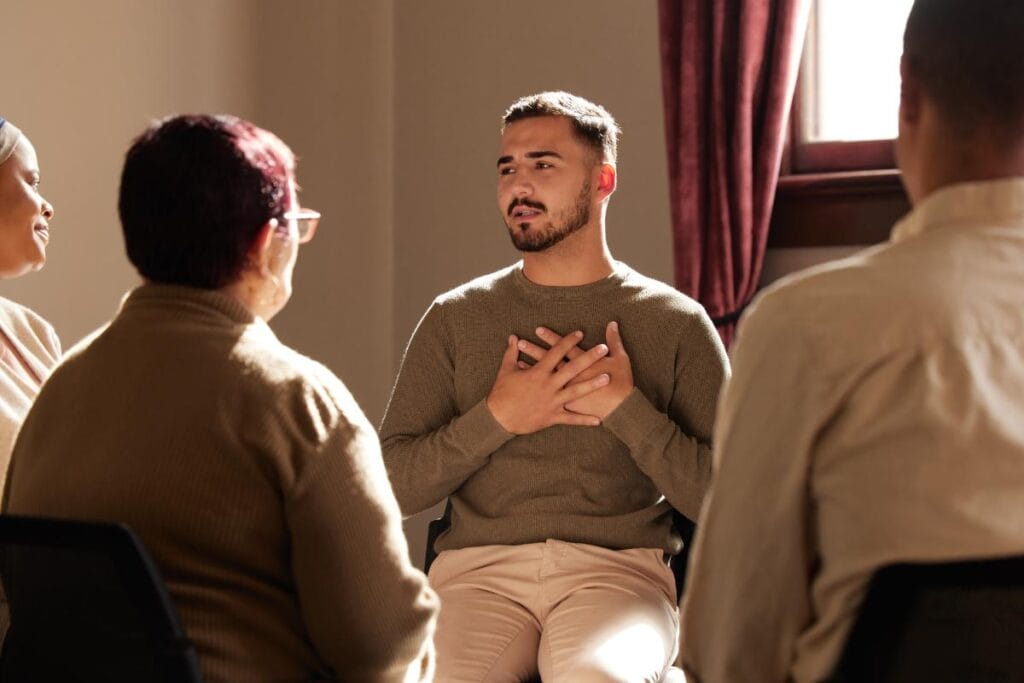 man holds his hands to his chest while expressing his thoughts in a group therapy session