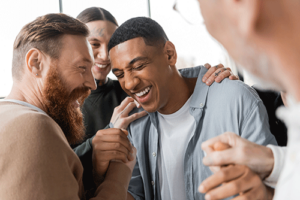 a group of men in a men's rehab program gather around one man and celebrate his successes