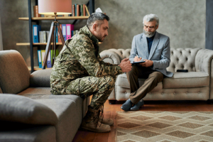 a service member in his uniform sits on a couch talking to his therapist in his veterans treatment