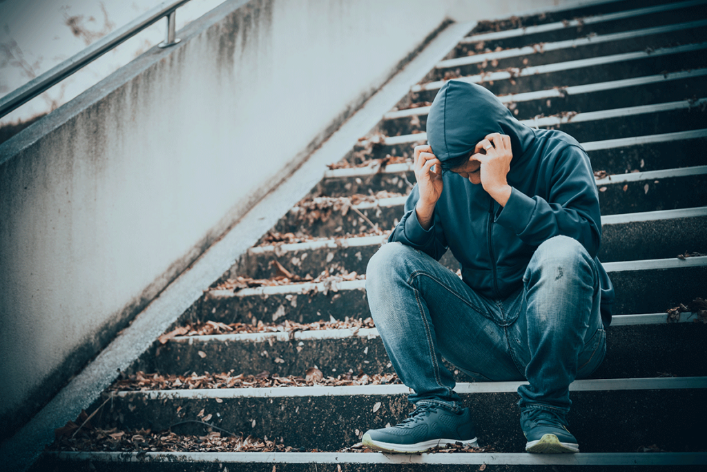 a person with their hood up and covering face sits on stairs struggling to understand the myths and facts about meth addiction
