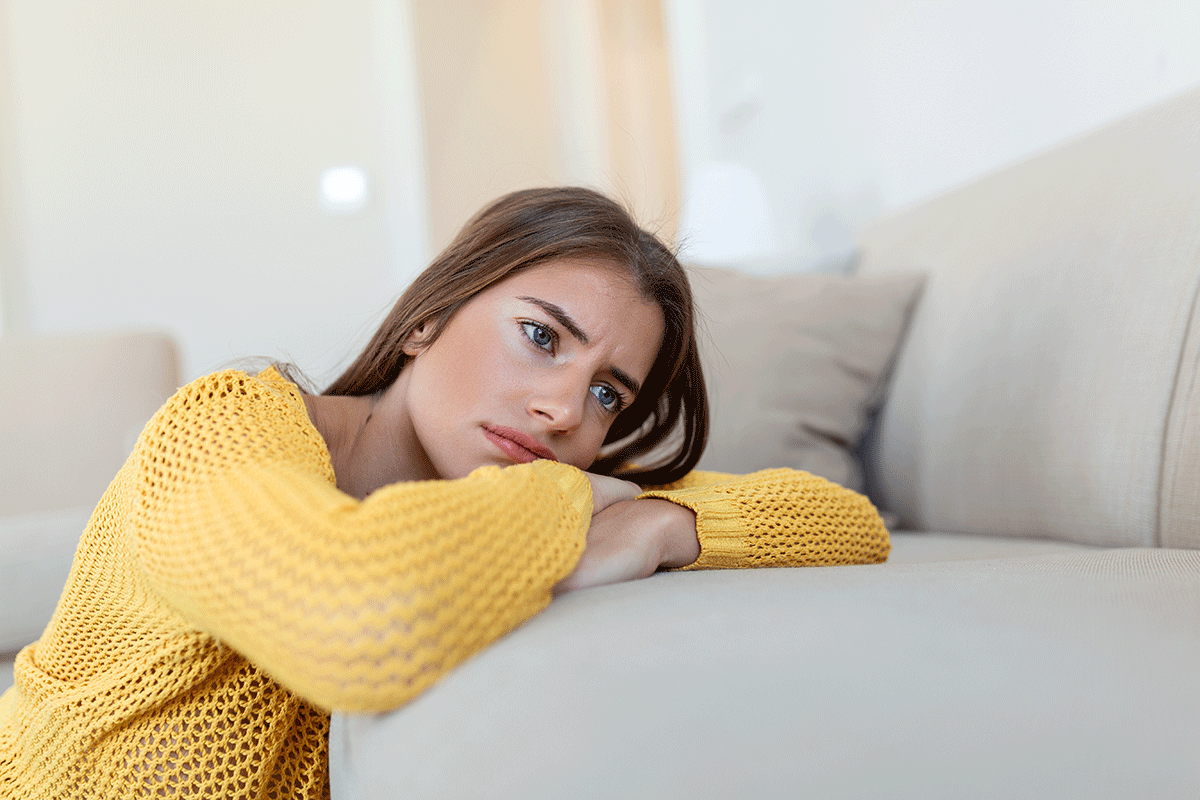 woman in yellow sweater lays her head on a couch cushion thinking about the symptoms of anxiety